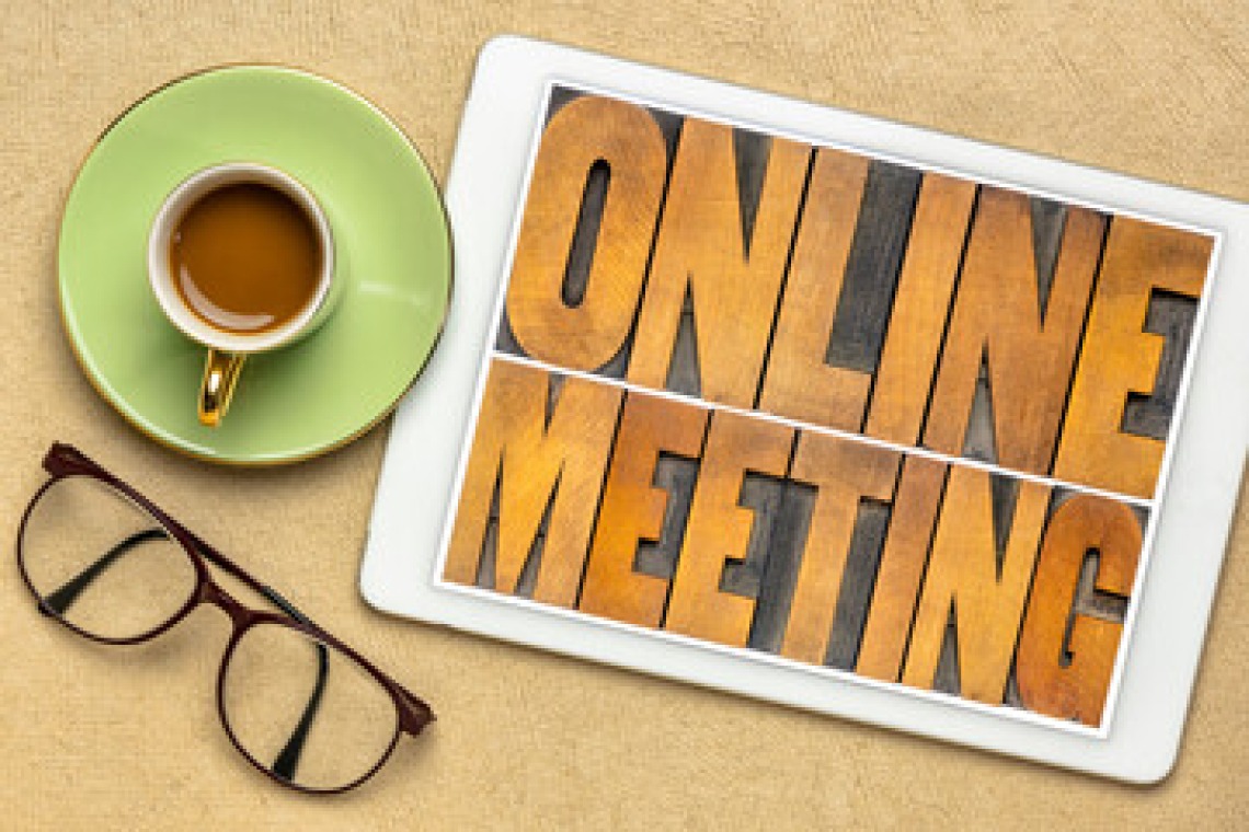 Table top holding a cup of coffee, a tablet that displays online meeting and reading glasses.